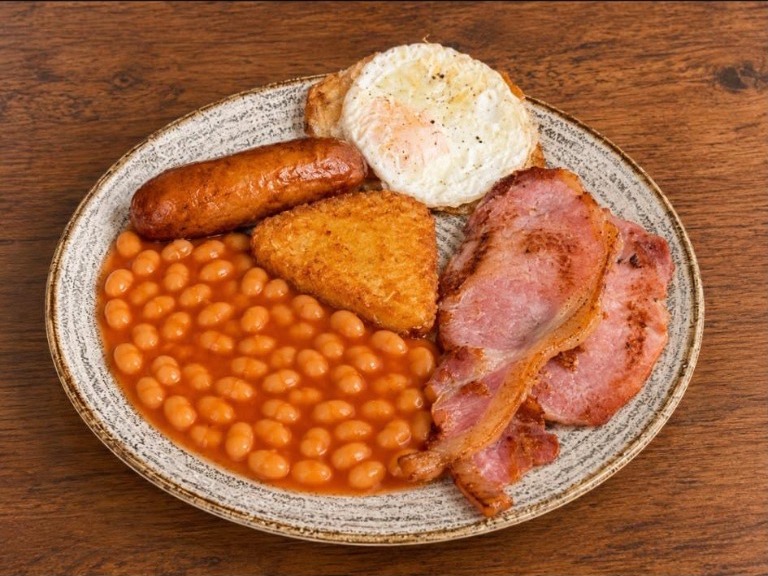 Bacon, sausage, a fried egg, hash brown and beans on a plate.
